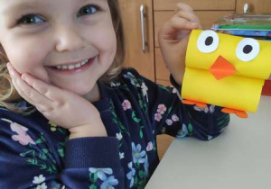 Uśmiechnięta dziewczynka trzyma zrobionego kurczaczka z żółtego papieru